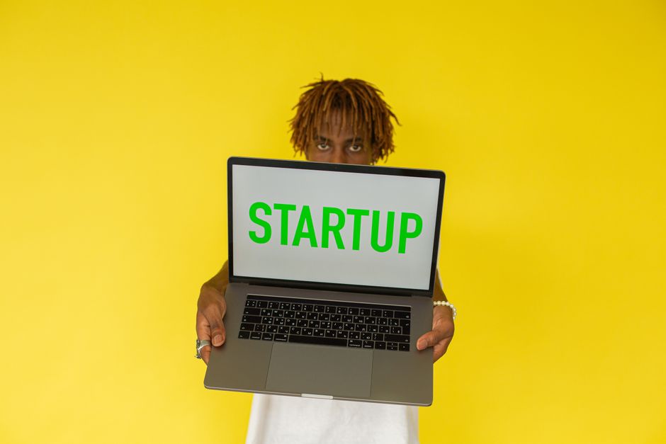 Joven sosteniendo una laptop con la palabra Startup sobre fondo amarillo vibrante